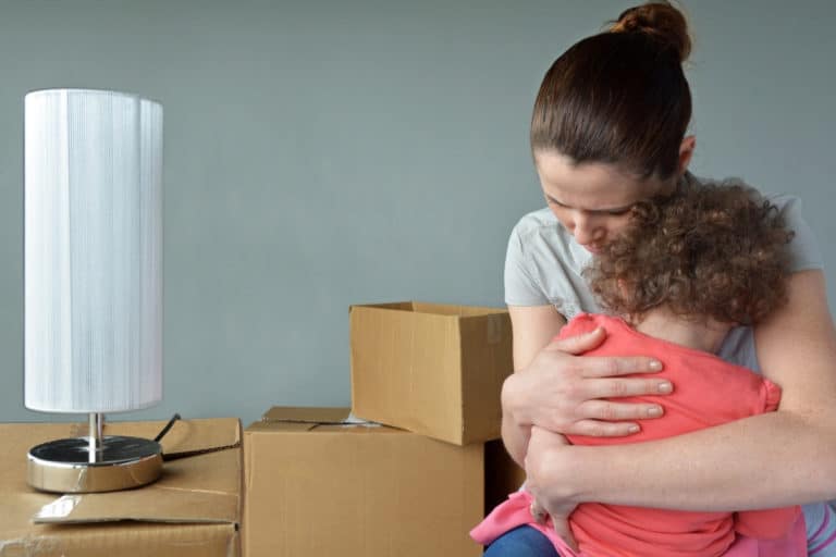 Mother hugging daughter in room with packing boxes and lamp