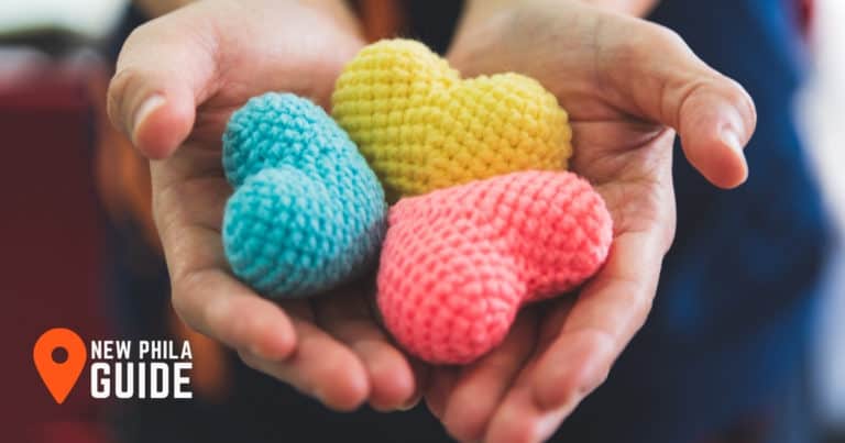 Hand holding a blue, pink and yellow hearts made out of yarn